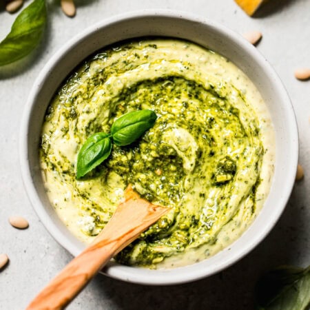 Homemade pesto mayo in bowl swirled with pesto and topped with basil leaf.