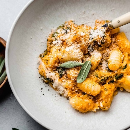 Pumpkin gnocchi in bowl topped with sage leaves.