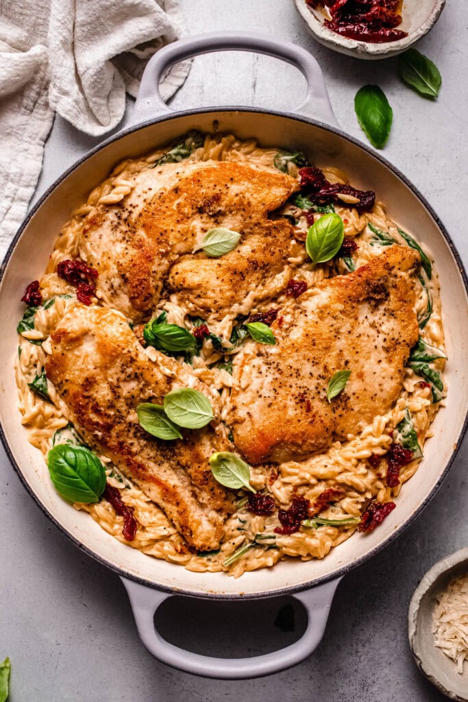 Chicken and sun dried tomato orzo in skillet topped with basil leaves.